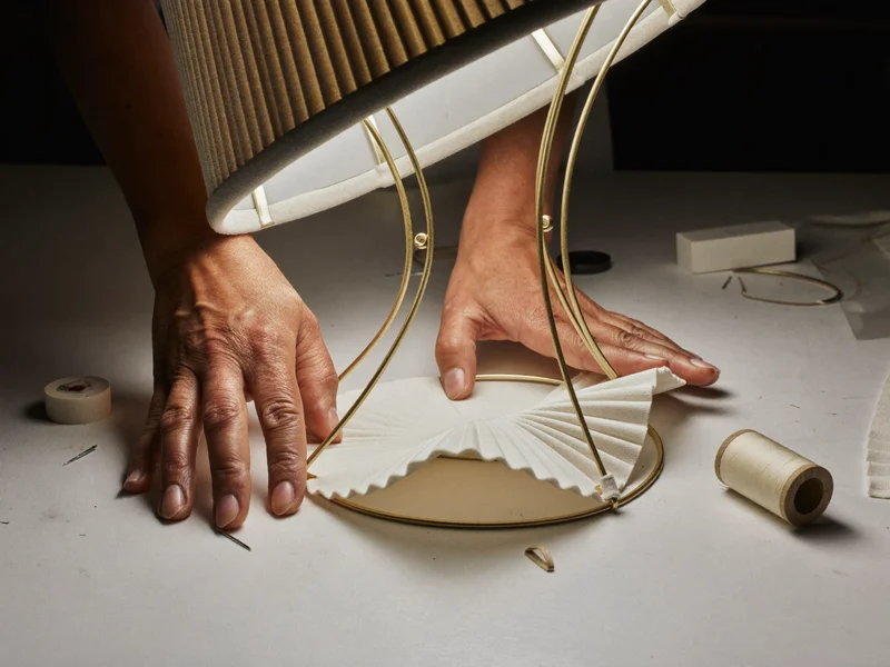 Mains d’artisan tendant un tissu plissé sur une armature d’abat-jour